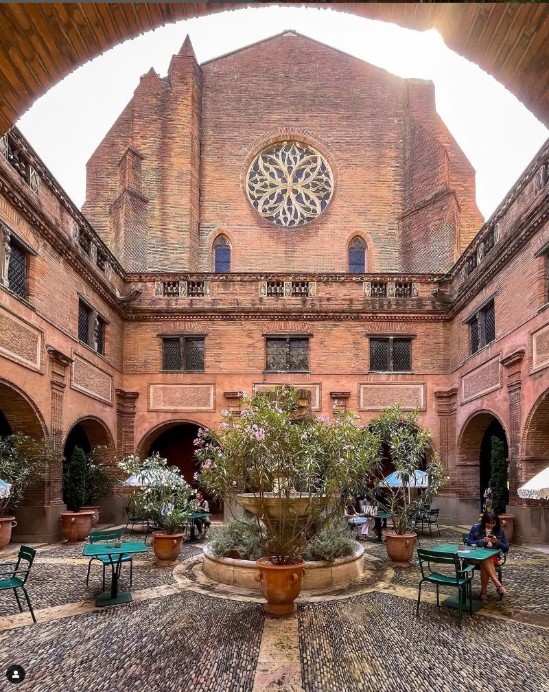 Vue du petit cloître du musée des Augustins avec la rosace de l'église côté ouest. Le petit cloître est orné de plantes et et aménagé avec des tables eet chiaises pour le repos du visiteur.