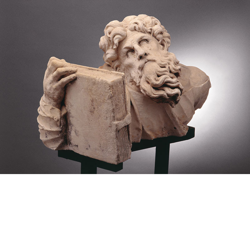 Buste en pierre d'un apôtre tenant un livre et pleurant, la tête penchée, cheveux et barbe bouclés.