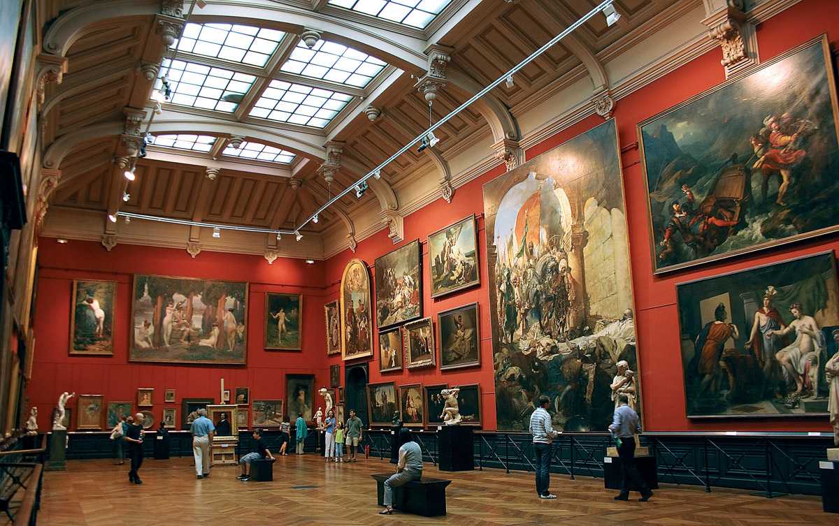 Vue du salon rouge surmonté d'une très grande et haute verrière. Vue des tableaux, notamment des grands formats.